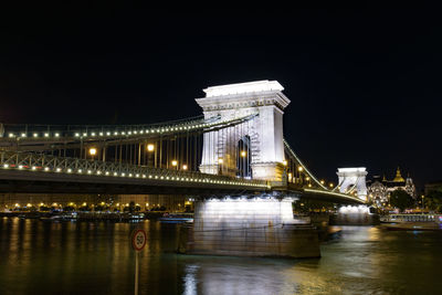 Illuminated bridge over river against sky at night