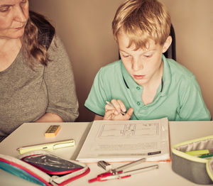 Mother teaching son while sitting by table at home