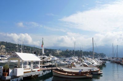 Boats in harbor against cloudy sky