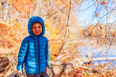 Portrait of boy wearing blue hooded jacket in forest during autumn