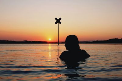 Rear view of silhouette woman swimming in lake against clear sky during sunset