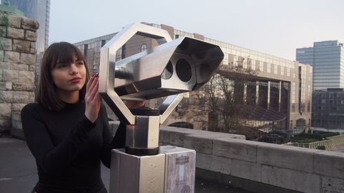 Woman standing by coin-operated binoculars in city
