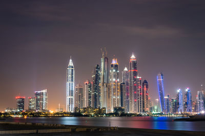 Illuminated modern buildings in city against sky at night