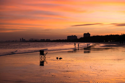 Silhoutte chair and sandals ob beach with happy family background at dusk with twilight sky, cha-am