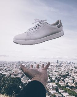 Close-up of hand throwing shoe against cityscape 