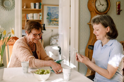 Smiling female caregiver is playing cards with senior woman at nursing home