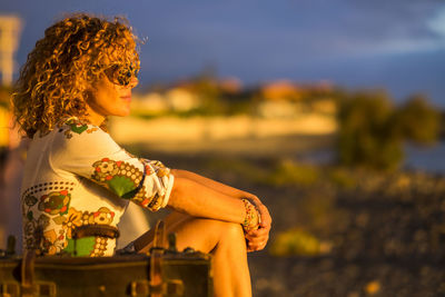 Side view of woman sitting on railing at beach during sunset