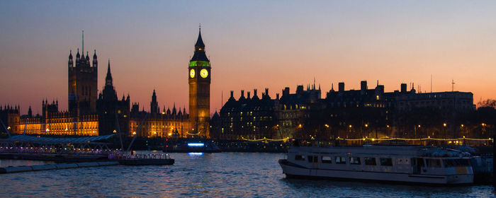 Panoramic view of illuminated big ben by thames river during sunset