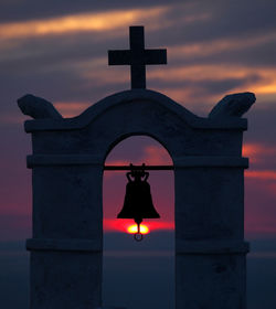 The sun sets through the bell tower of the chapel of agios nikolaos, ios, greece