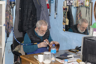 Senior man carving on brass container while sitting in workshop