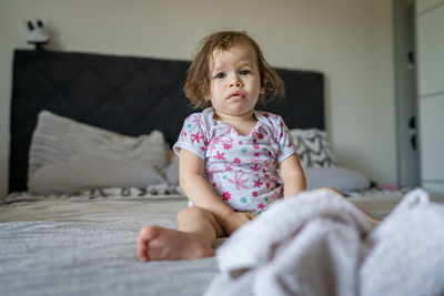 Portrait of cute baby boy sitting on bed at home