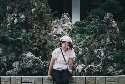 Portrait of young woman standing on rock against trees