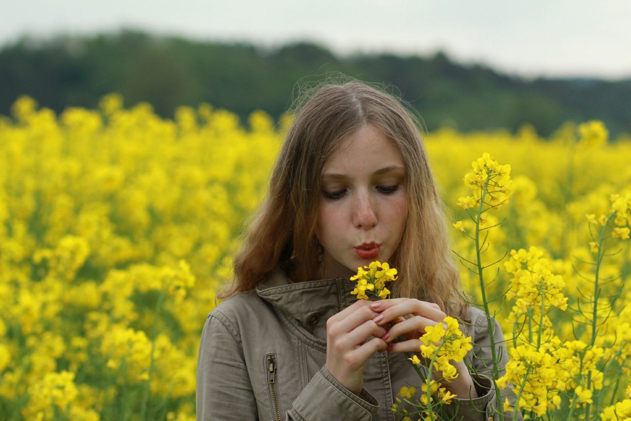 flower, person, yellow, focus on foreground, lifestyles, freshness, field, leisure activity, beauty in nature, young adult, nature, growth, casual clothing, young women, fragility, waist up, smiling, long hair