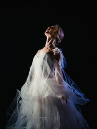 Ballet dancer wearing white dress dancing against black background