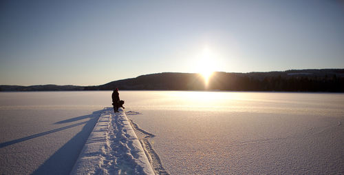 Woman on snow covered mountain against sky during sunset