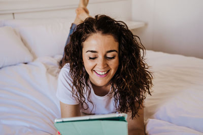 Smiling woman using digital tablet while lying on bed at home