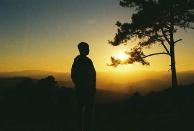 Silhouette man standing by tree against orange sky