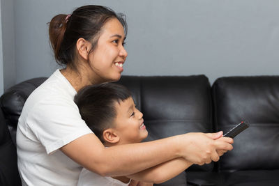 Smiling mother and son watching tv while sitting on couch at home