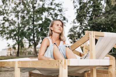 Thoughtful woman sitting on deck chair against trees