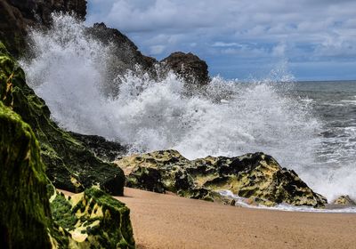 Waves breaking on rocks at shore against sky