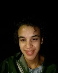 Close-up portrait of smiling young woman against black background