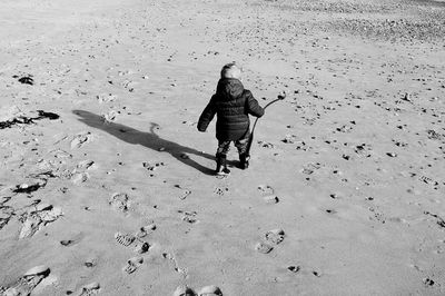 Rear view of kid walking with shadow on wet shore at beach