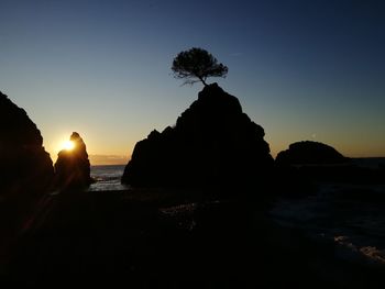 Silhouette rocks on beach against sky during sunset