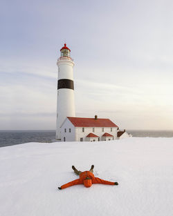 Male hiker relaxing on snow covered mountain while lighthouse in background