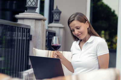 Smiling woman holding wineglass using laptop