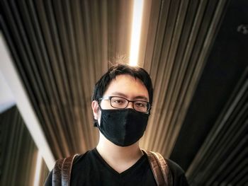 Portrait of young man standing against ceiling and wall.