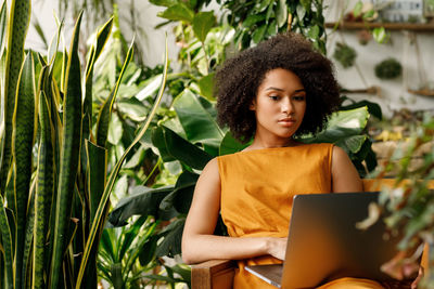Young woman using laptop while sitting on chair against plants