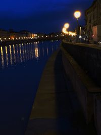Illuminated street lights by river in city at night