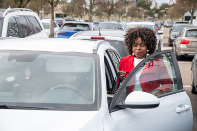 African american woman in red coat opens doors to get into a white car