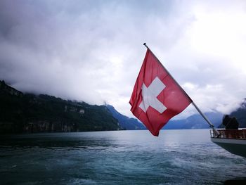 Swiss flag on boat in lake against cloudy sky