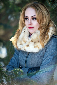 Young woman wearing winter coat and standing in evergreens