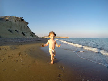 Toddler baby playing on a sandy beach and running among sea waves