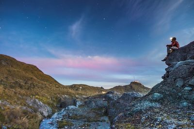 Low angle view of man sitting on rocky mountain against sky