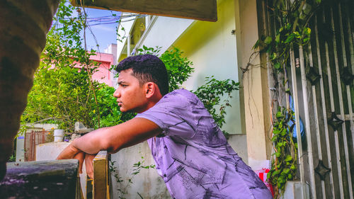 Side view of young man standing against gate