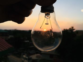 Close-up of hand holding light bulb at sunset