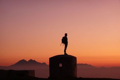 Silhouette man standing on built structure against orange sky