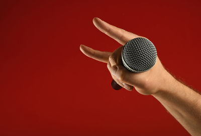 Cropped image of singer holding microphone with hand sign against red background