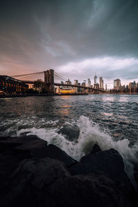 View of suspension bridge over river against cloudy sky