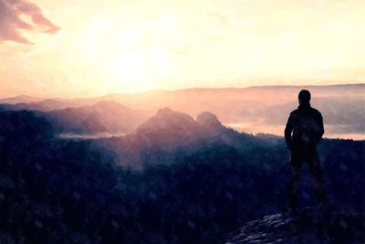 Rear view of man looking at mountains against sky during sunset