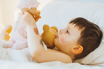 Young boy lying in bed playing with a doll