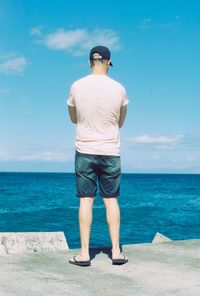 Rear view of man looking at sea against sky during sunny day