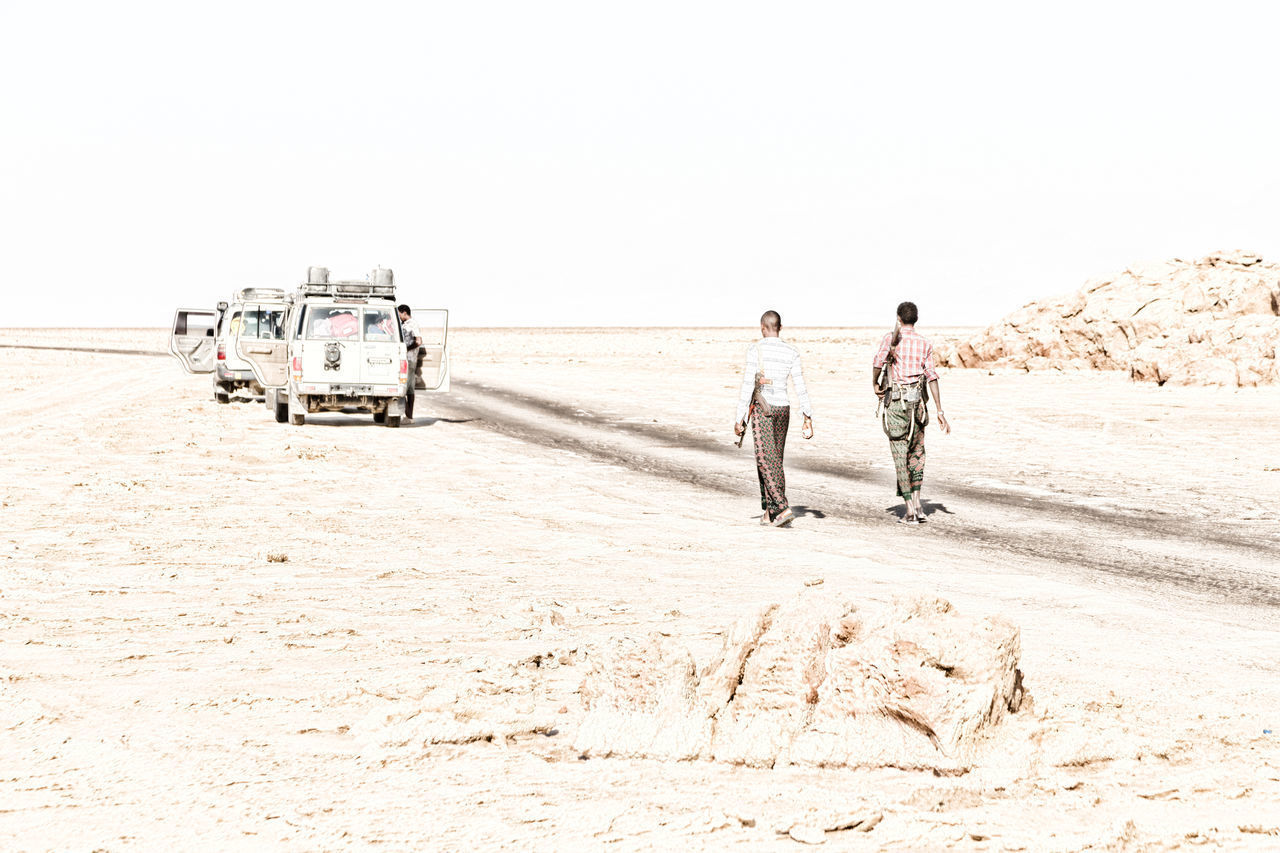 REAR VIEW OF PEOPLE WALKING ON SANDY BEACH