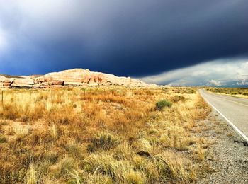 Road passing through field against cloudy sky