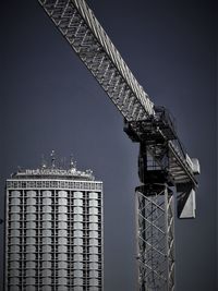 Low angle view of crane by building against sky