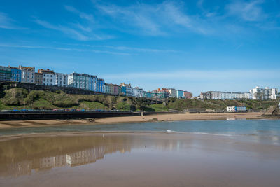 Buildings by river against blue sky