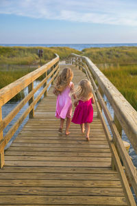 Little girls from behind running on bridge to beach in pink dresses